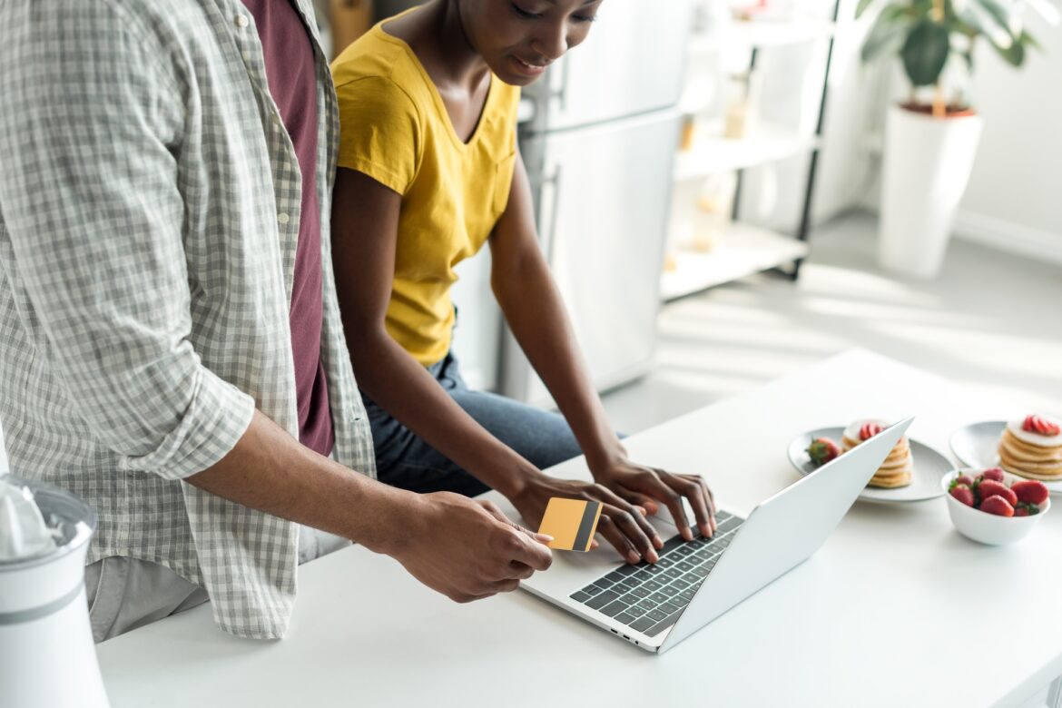 cropped image of african american couple shopping online with credit card and laptop at kitchen